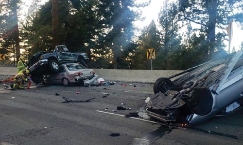 A bad car accident with a pickup truck sitting on top of a crumpled car